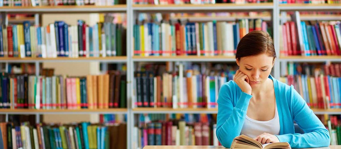 portrait-of-clever-student-with-open-book-reading-it-in-college-library_1200x628